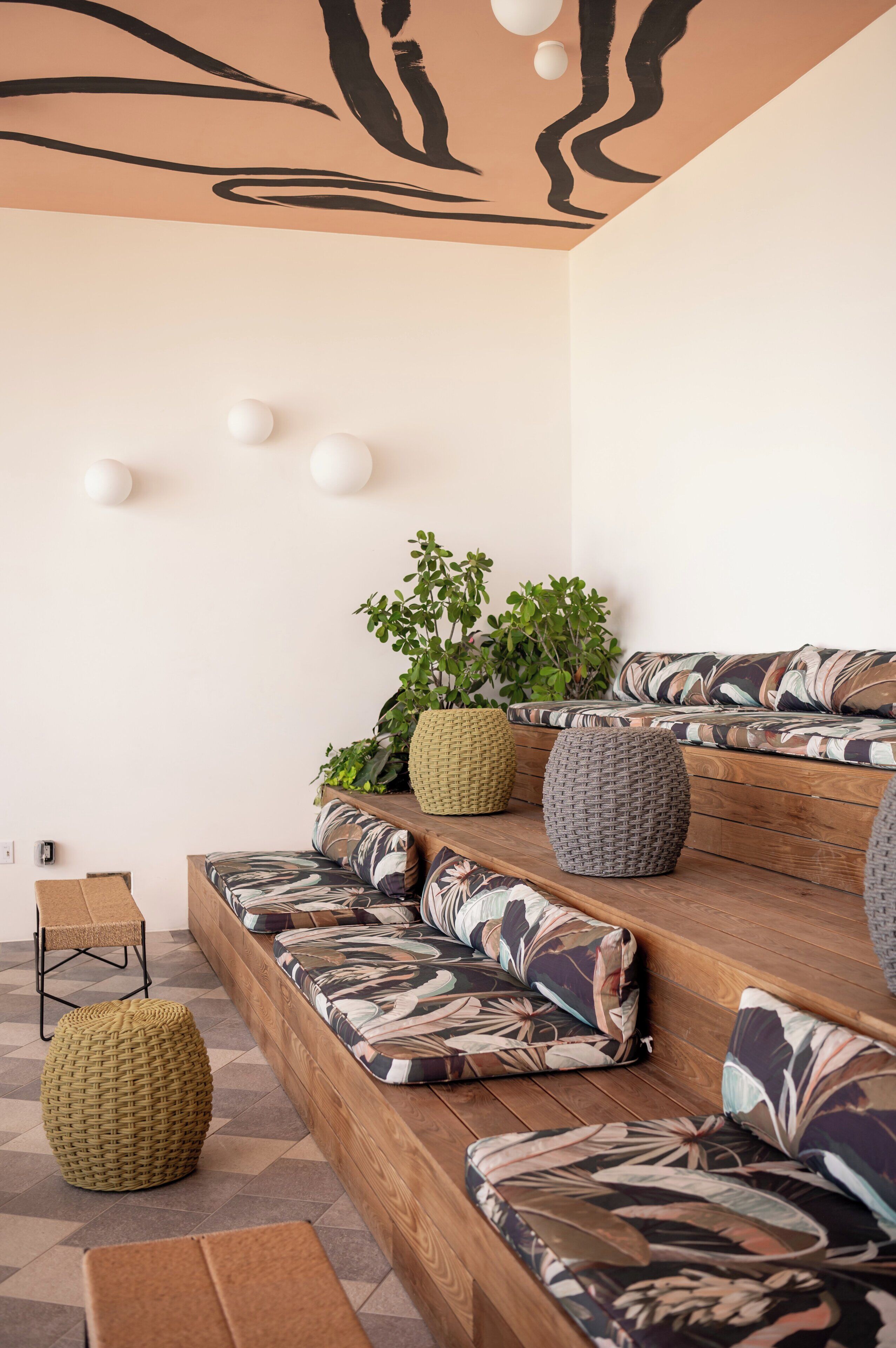 A modern seating area with a wooden bench and cushioned seating, surrounded by potted plants and decorative spheres on the wall.