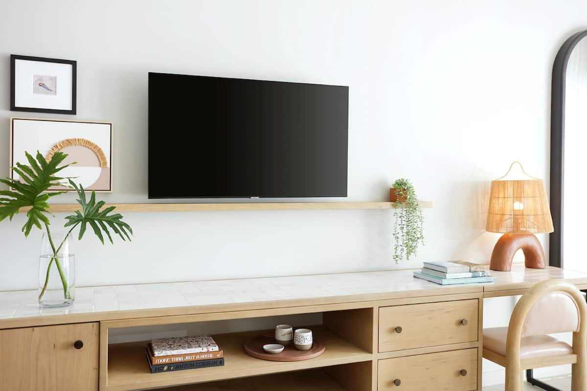 A modern workspace with a flat-screen TV, a wooden desk, a chair, a lamp, and a small plant.