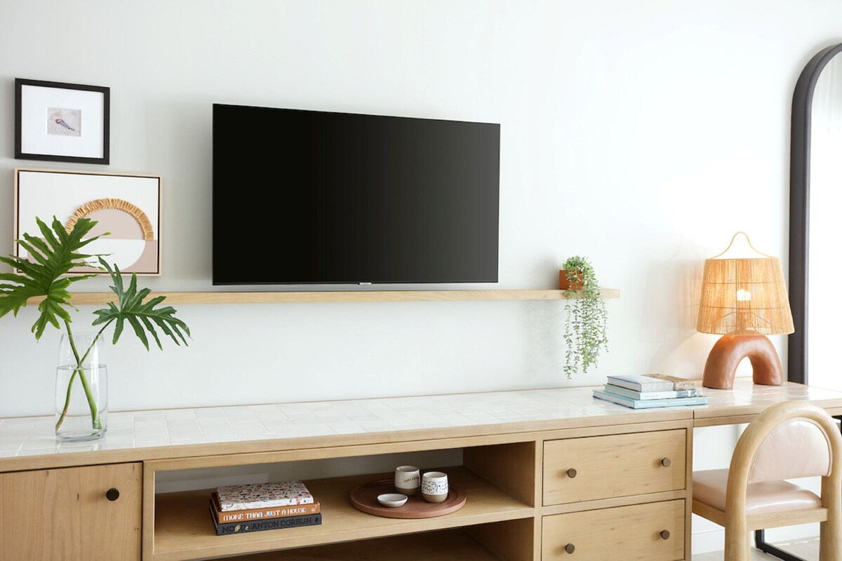 Un espacio de trabajo moderno con una televisión de pantalla plana, un escritorio de madera, una silla, una lámpara y una planta pequeña.