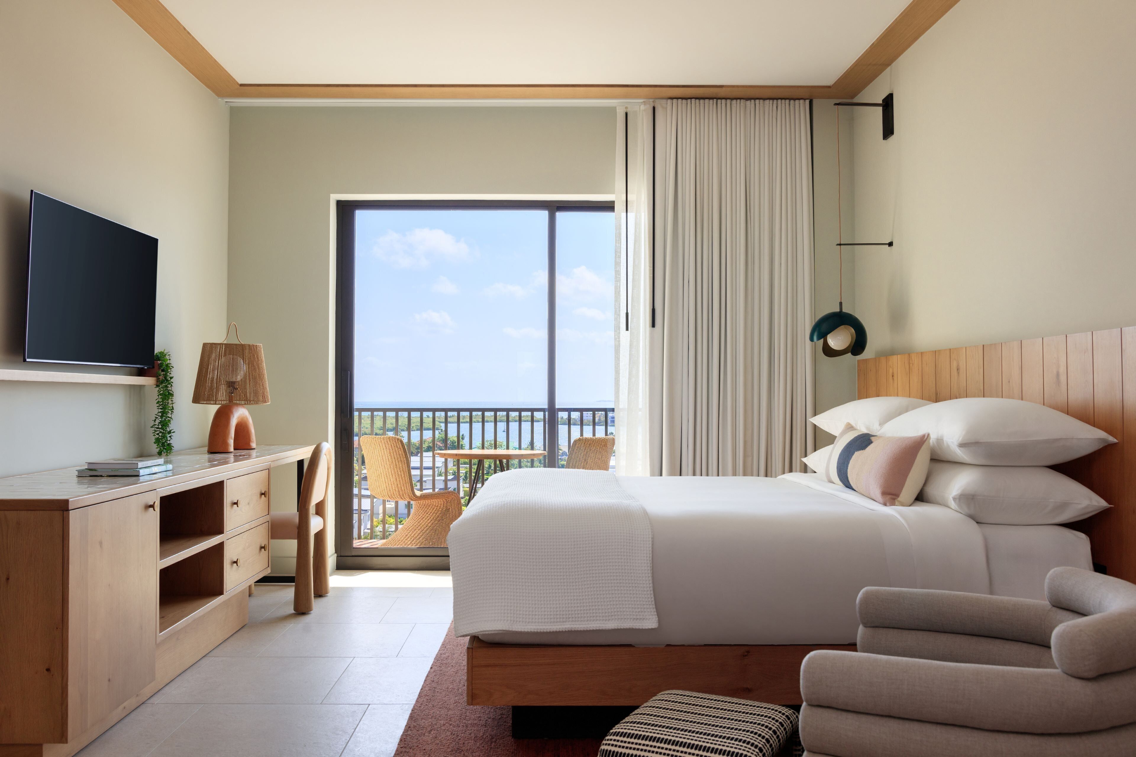 A hotel room with a bed, a desk, a TV, and a balcony with a view of the sea.