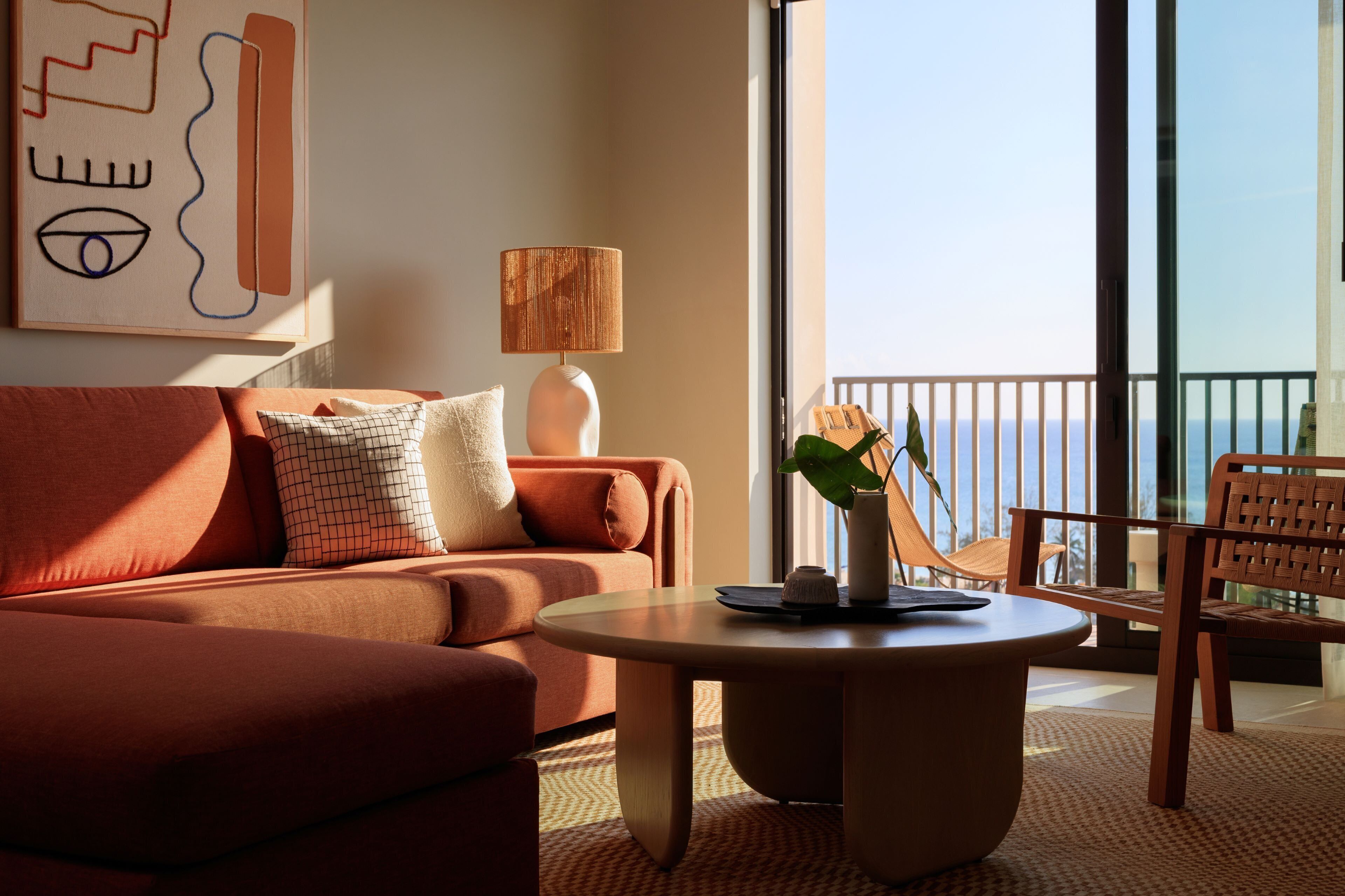 Un salon moderne avec un canapé, une table basse ronde et une vue sur la mer grâce à de grandes fenêtres.