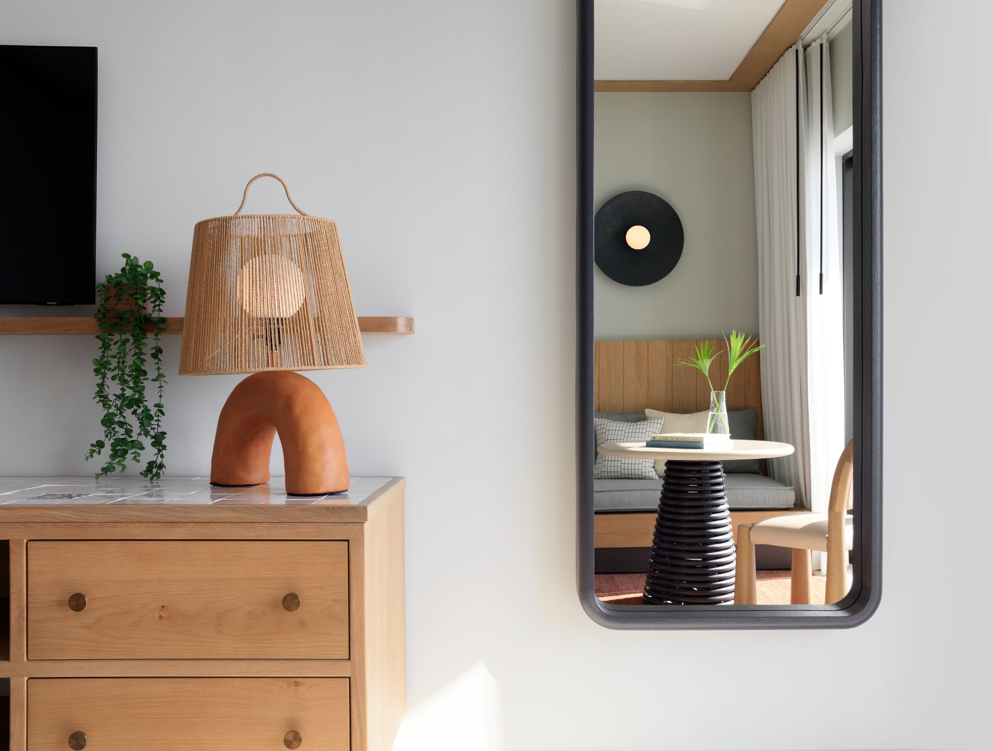 Una habitación moderna con un armario de madera, una lámpara trenzada, una planta y vistas a un sofá y una mesa a través de una ventana.