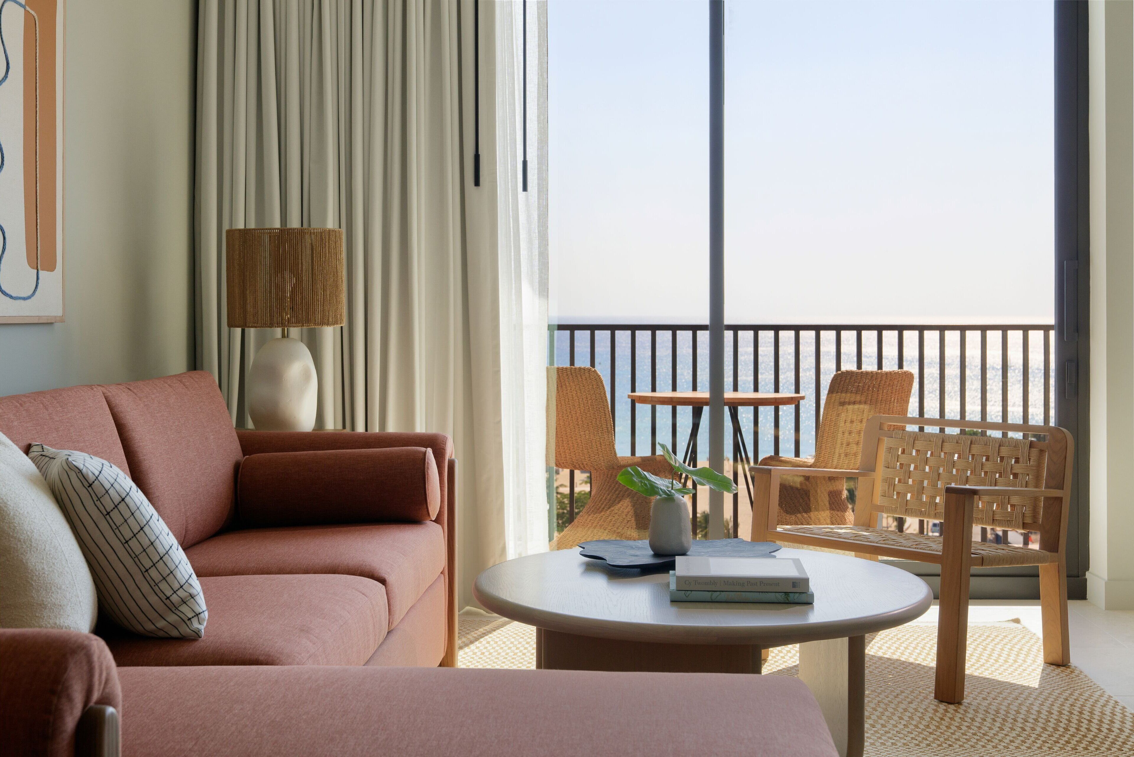 A modern living room with a sofa, a coffee table, and a view of the sea through a balcony.