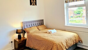 Une chambre à coucher avec un lit, une lampe de chevet, un tableau accroché au mur et une fenêtre donnant sur l’extérieur.