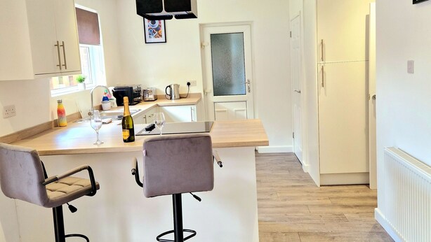 Une cuisine moderne avec des meubles blancs, un plan de travail en bois et un coin repas avec une table dressée pour deux personnes.
