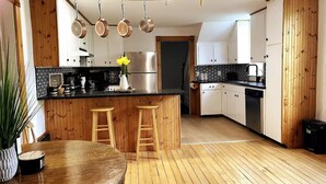 A modern kitchen with wooden accents, a central island with stools, hanging pots, and a stainless steel refrigerator. - Rustic cabin-inspired residence.
 (Caledon)
