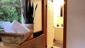 A wooden chest with towels and a potted plant by a window. A door leads to a bathroom with a sink and mirror. - Rustic cabin-inspired residence.
 (Caledon)