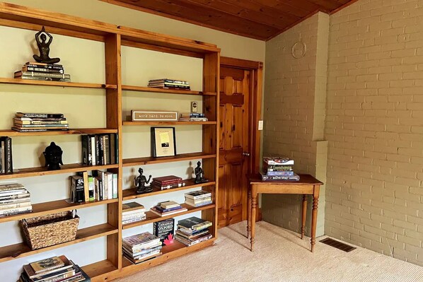 A room with a wooden bookshelf filled with books and decorative items, a small wooden table with books and a box, and a brick wall. - Rustic cabin-inspired residence.
(Caledon)