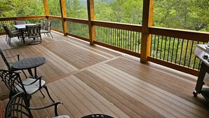 Eine überdachte Terrasse im Freien mit Holzboden, Metallstühlen, einem Tisch und einem Grill.