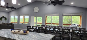 Un espace repas comprenant une table en marbre, des chaises, un ventilateur de plafond et de grandes fenêtres donnant sur un paysage verdoyant.