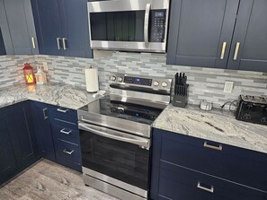 A modern kitchen with dark cabinetry, a stainless steel microwave, a built-in oven, and a stovetop. - Heart of Branson Retreat / Hot Tub / Pool Table / Game Room / Fire Pit / Lvl2 EV (Branson)