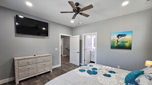 Ein Schlafzimmer mit Bett, Kommode, Deckenventilator, Fernseher und einem Gemälde.