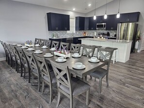 Une cuisine moderne avec des meubles sombres, un îlot central et un coin repas comprenant des chaises en bois et une table dressée pour six personnes.