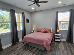 A bedroom with a bed, two bedside tables, a ceiling fan, and a window with curtains.