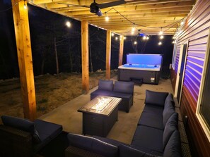 An outdoor patio with a hot tub, seating area, and string lights.