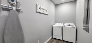 Une buanderie équipée de deux machines à laver Samsung blanches, d’un panneau fixé au mur et d’un porte-serviettes.