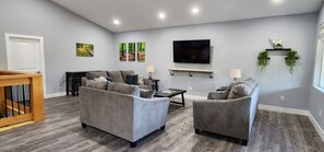 Ein Wohnzimmer mit grauen Sofas, einem Couchtisch, einem Fernseher und Kunstwerken an der Wand.