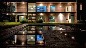 A modern two-story house with a glass facade, a stone pool, and outdoor lighting.