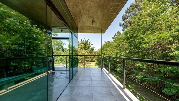 A modern balcony with glass railings, a concrete ceiling, and a view of lush greenery.