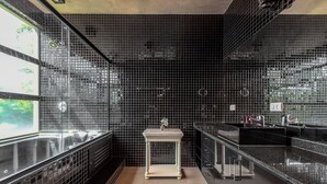 Un baño moderno con paredes de azulejos negros, un lavamanos blanco pedestal y un amplio ventanal que proporciona luz natural.