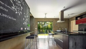 A modern kitchen with a chalkboard wall, bar stools, and a view of greenery outside.