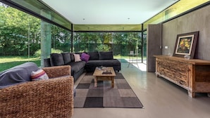 A modern living room with a large glass wall, a black sofa, a wooden coffee table, and a rustic wooden cabinet.