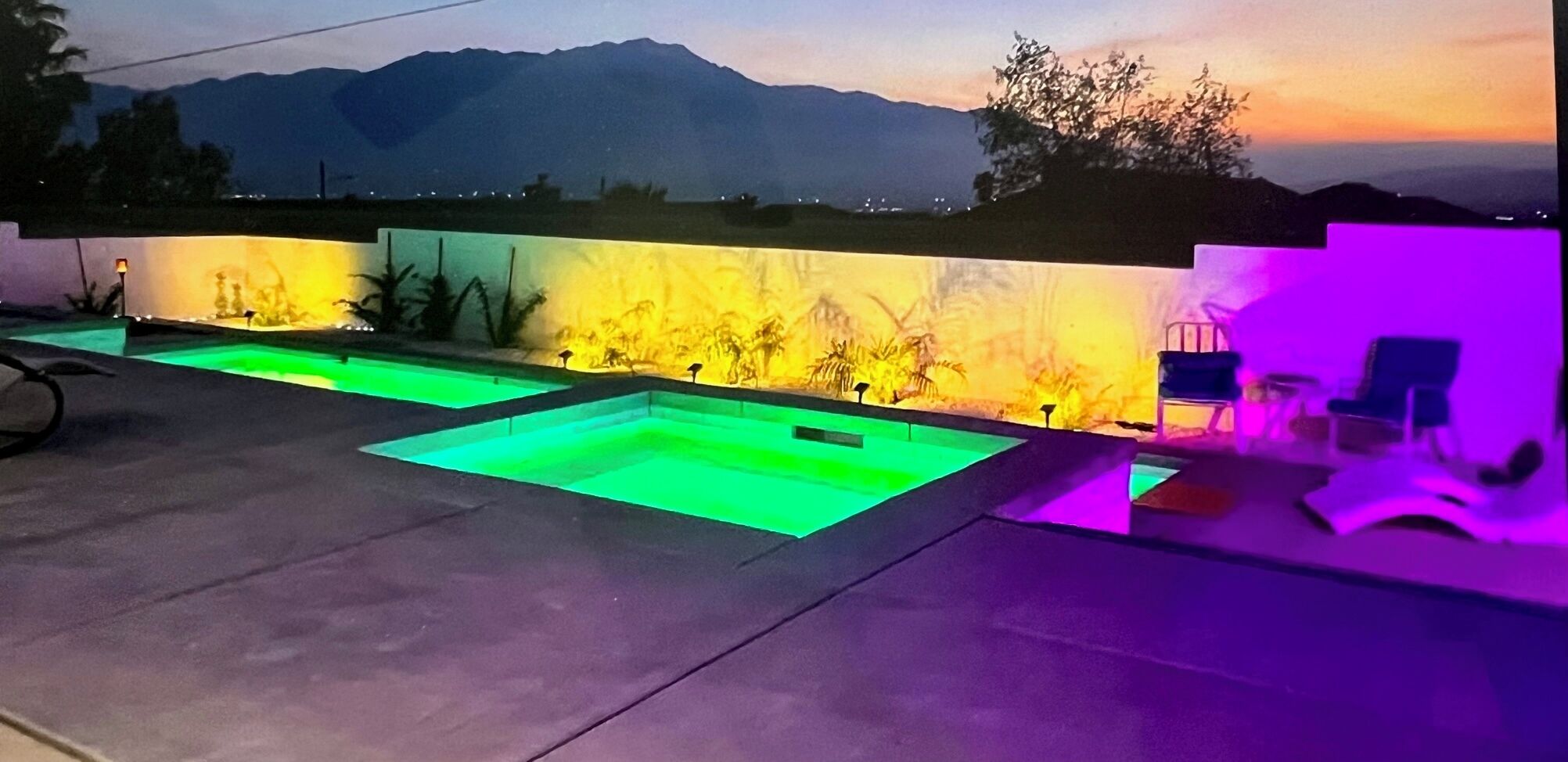 Zona de piscina en la azotea con vistas a montañas al atardecer, un espacio de descanso con sillas y una pared con un mural.