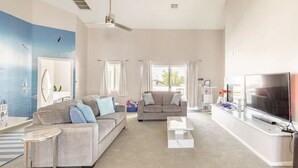 A spacious living room with a large TV, two sofas, a coffee table, and a ceiling fan.