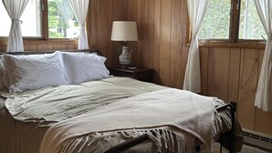 Un dormitorio con cama, cortinas, una mesita de noche con lámpara y paredes de madera.