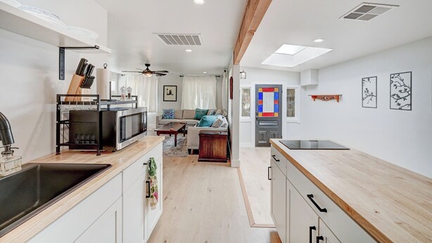 Una cocina moderna con una isla central, una zona de comedor con sofá y un pasillo que conduce a una puerta con un vitral colorido.