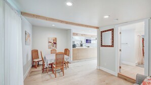 Un espacio habitable amplio con una mesa de comedor y sillas, una cocina al fondo, y una puerta que da a otra habitación.