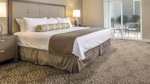 Una habitación de hotel con una cama grande, una mesita de noche, una lámpara y vistas al exterior a través de una puerta corrediza de vidrio.