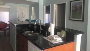 A modern kitchen with a black countertop, stainless steel sink, and a dish drying rack. - Luxurious 1BR Condo for Coachella Week 2 (Indio)