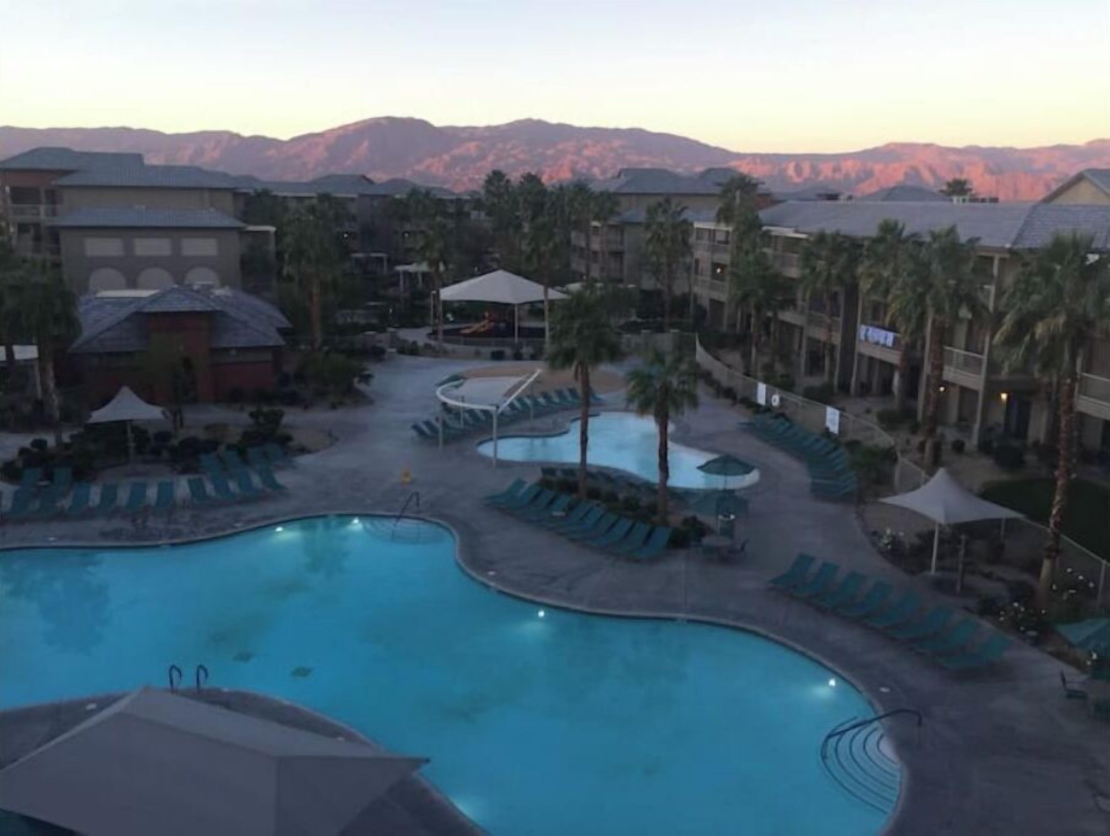 A resort pool area with multiple pools, lounge chairs, and palm trees.