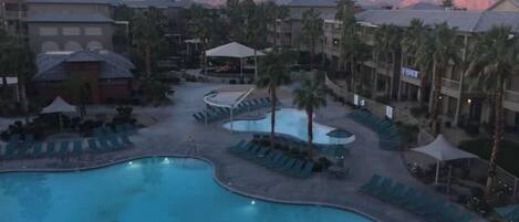 A resort pool area with multiple pools, lounge chairs, and palm trees.