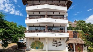 Un immeuble à plusieurs étages doté de balcons, orné d’une fresque représentant un paon, et sur lequel on peut lire l’inscription : « À un kilomètre de Saymua ».