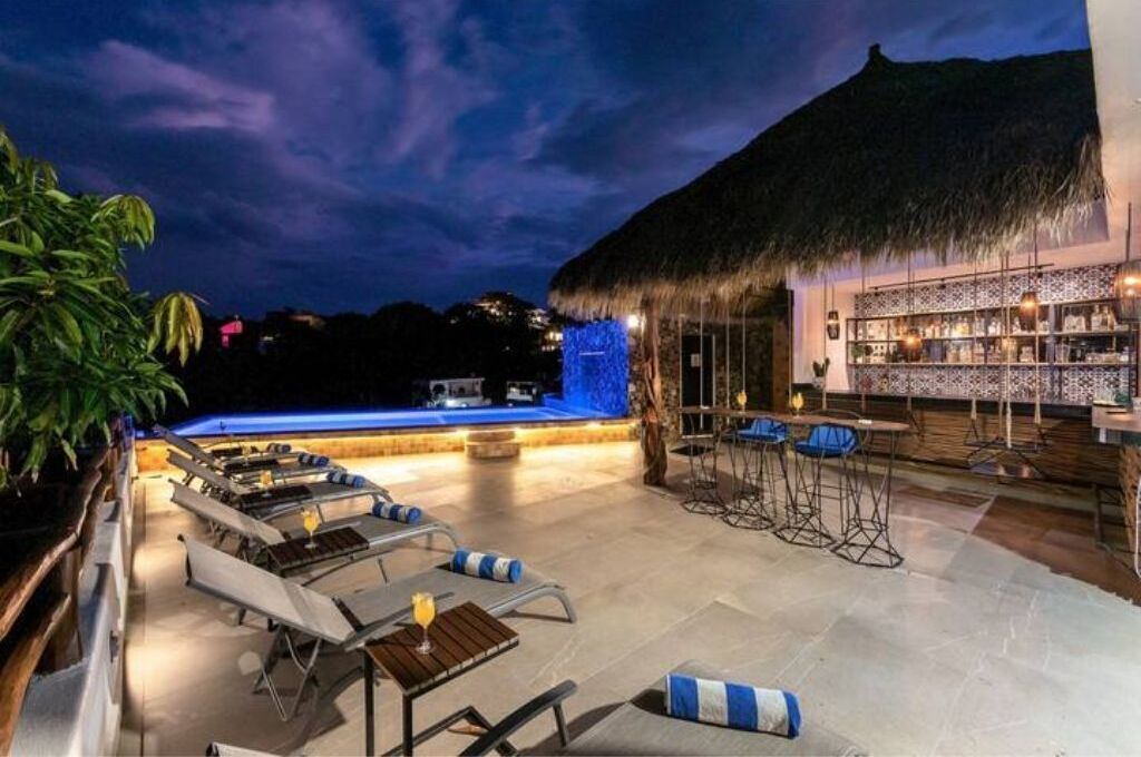 An outdoor bar area with a thatched roof, lounge chairs, and a pool with blue lighting.