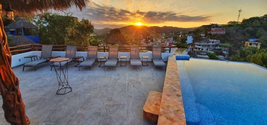 Une terrasse sur le toit, dotée de chaises longues et d’une piscine, offrant une vue imprenable sur un magnifique coucher de soleil.