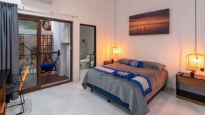 Un dormitorio con cama, lámparas de noche, un cuadro y un puerta corredera que da a un balcón con una silla.