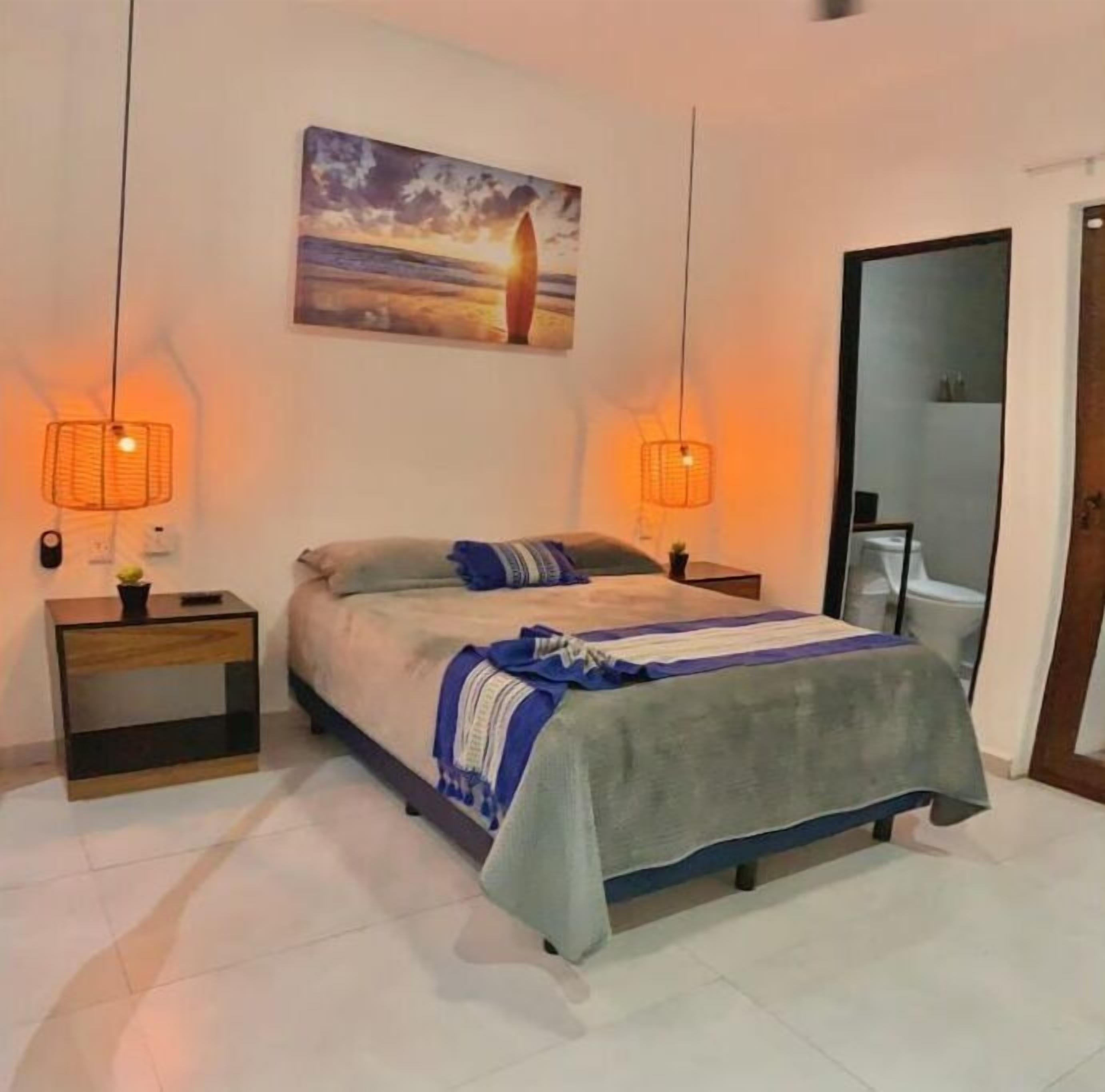 A bedroom with a bed, nightstands, a painting, and a mirror.