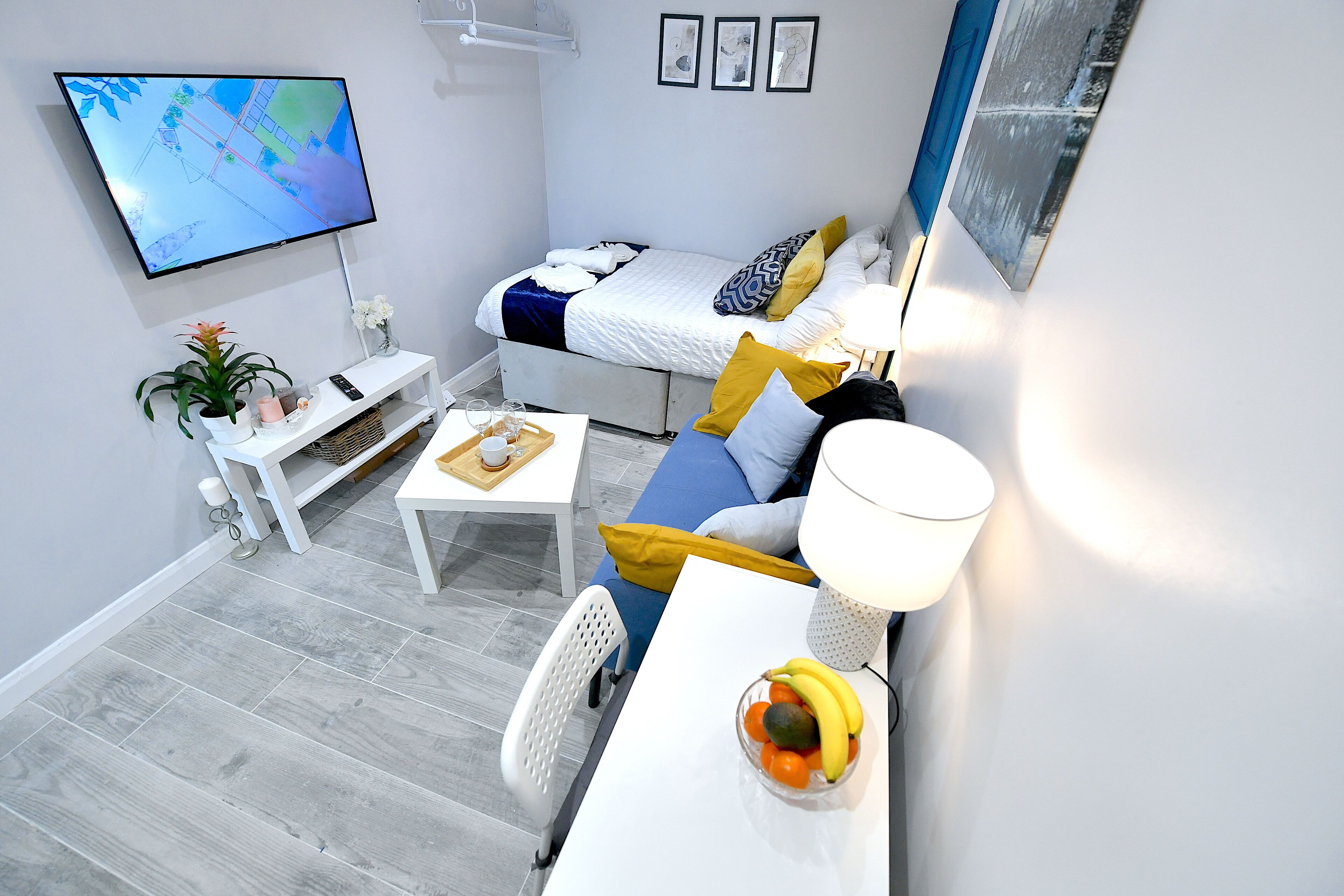 Une chambre compacte et moderne, équipée d’un lit, d’un canapé, d’une petite table et d’un téléviseur fixé au mur.