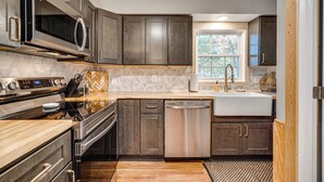 A modern kitchen with dark wood cabinets, stainless steel appliances, and a large window providing natural light. -  Mountain Views/Hot tub/Sauna/Game Room/Fire Pit (Shenandoah)