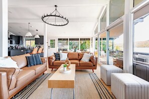 Een ruime woonkamer met een bruine leren bank, een houten salontafel en een groot raam met uitzicht op de natuur.