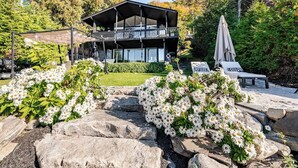Un edificio moderno con balcón, rodeado de un jardín con flores blancas y rocas.