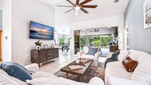 A spacious living room with a large flat-screen TV, a ceiling fan, and a view of the outdoors through glass doors. - LUXURY Villa AZUL Naples with HEATED SALT WATER POOL (Naples)