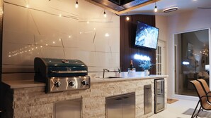 A modern kitchen with a built-in grill, stainless steel appliances, and a flat-screen TV mounted on a wooden panel wall. - LUXURY Villa AZUL Naples with HEATED SALT WATER POOL (Naples)