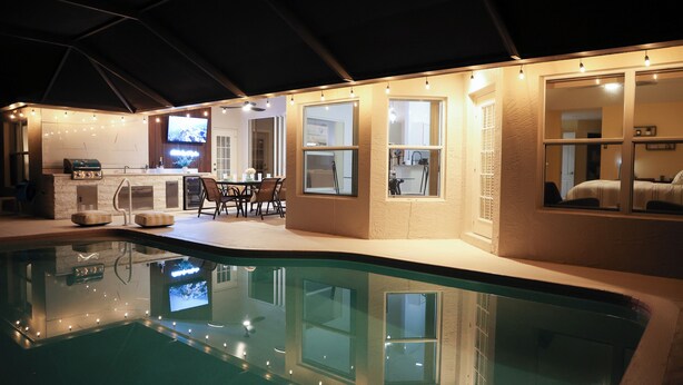A pool area with a bar and seating, surrounded by walls with windows and a television. - LUXURY Villa AZUL Naples with HEATED SALT WATER POOL (Naples)