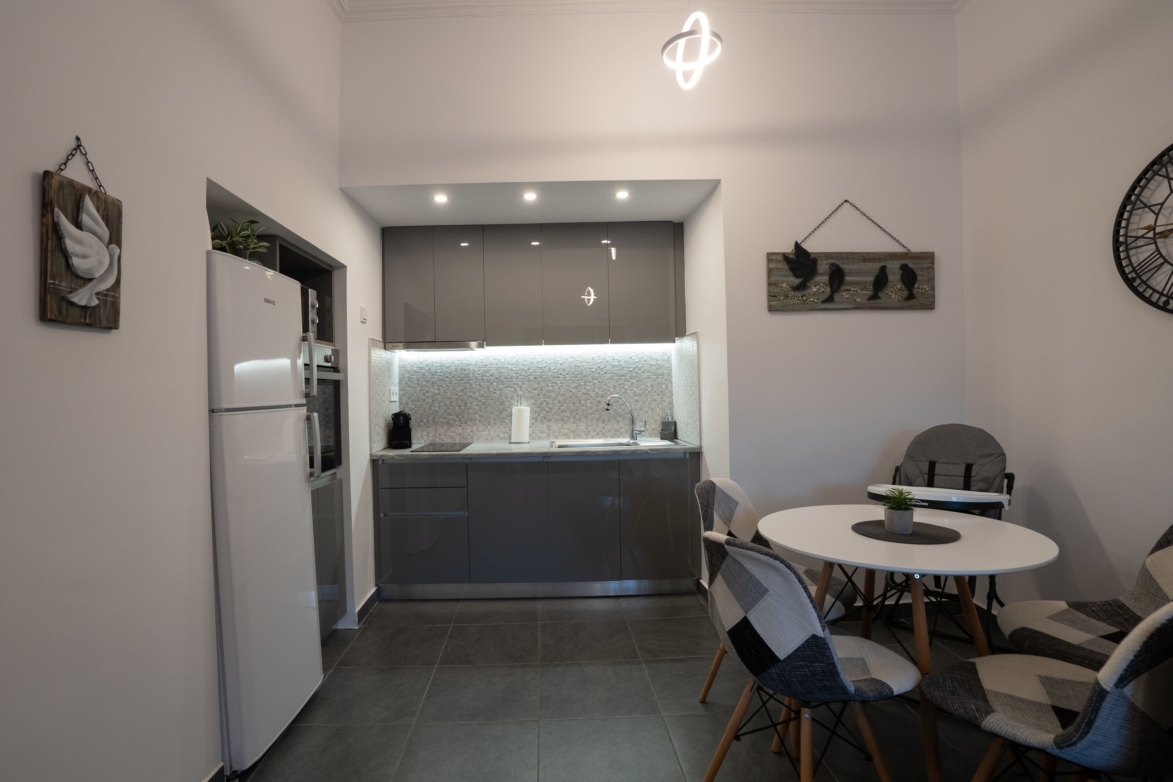 Eine kompakte Küche mit modernem Design, inklusive Einbaukühlschrank, Spüle und einer Essecke mit rundem Tisch und Stühlen.