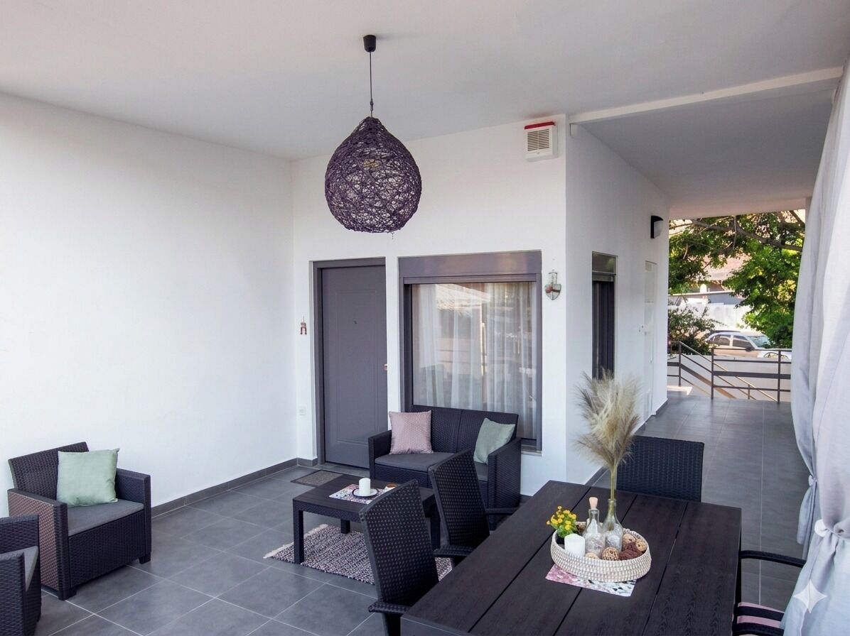 A modern outdoor seating area with dark furniture, a hanging light fixture, and a view of the street.