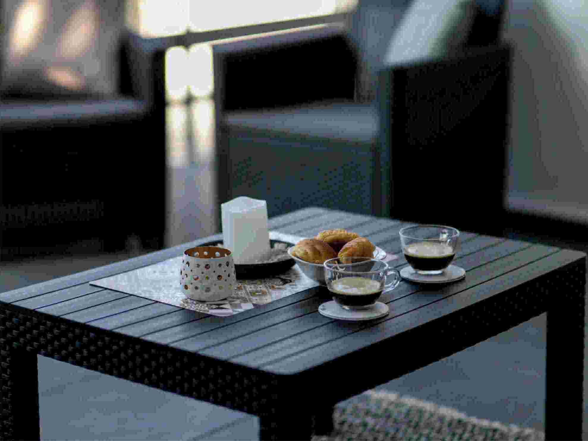 A table with a candle, a cup, a plate with pastries, and a glass of coffee.